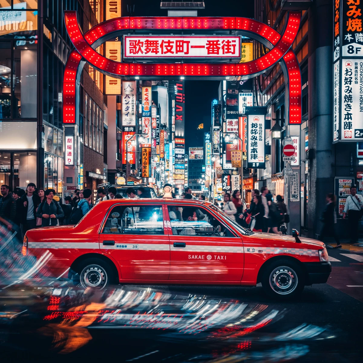 Rotes Taxi auf einer belebten Straße in Tokio, Japan, mit leuchtenden Neonlichtern und japanischen Schriftzeichen im Hintergrund des nächtlichen Stadtviertels.